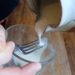 Pouring kefir over fork tines to catch kefir grains remaining in kefir